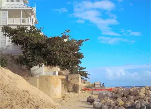 A large pile of sand lies on the beach next to boulders