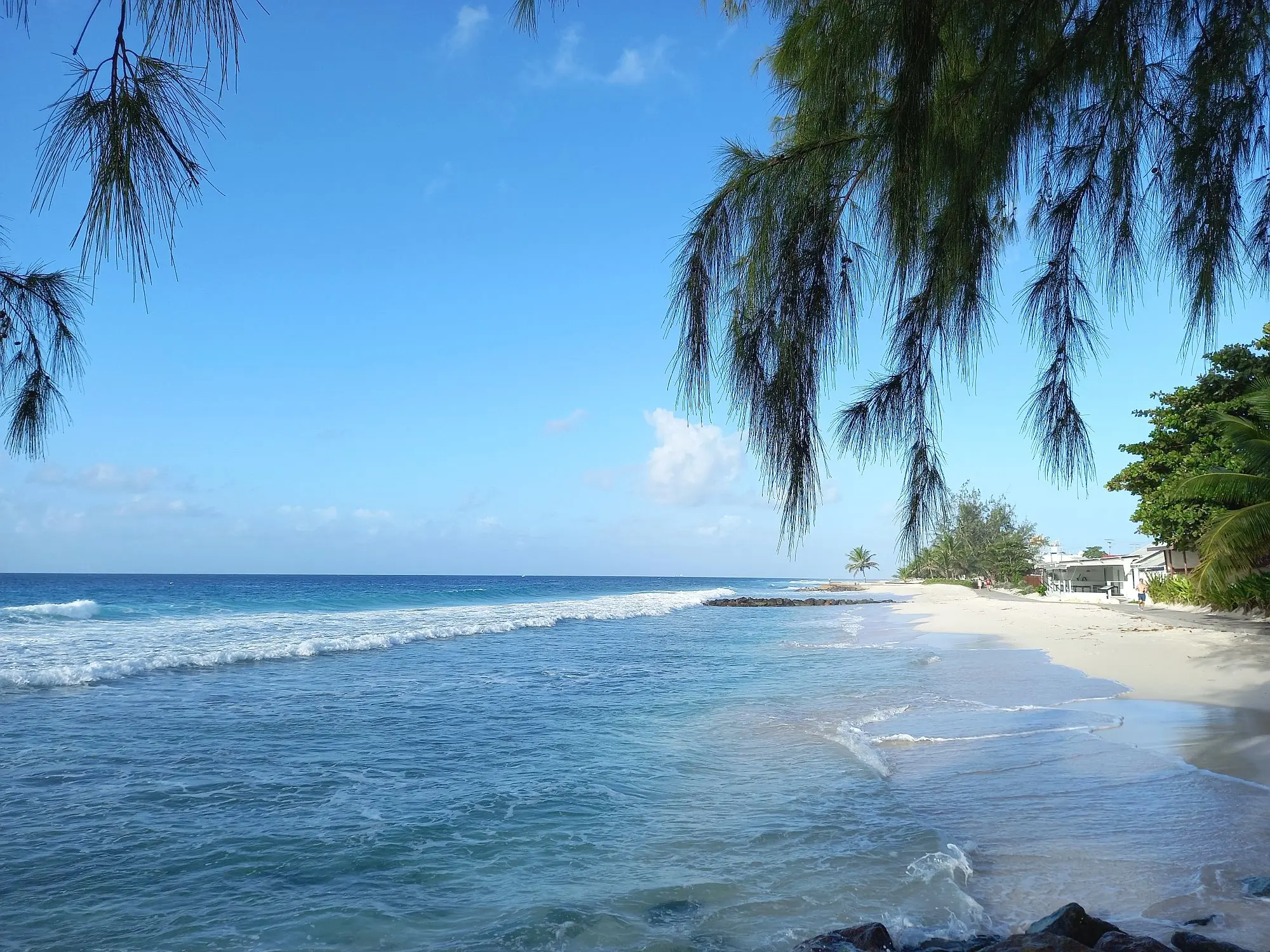 Wide white-sand beach with gentle waves breaking on the shore, to the left of the boardwalk